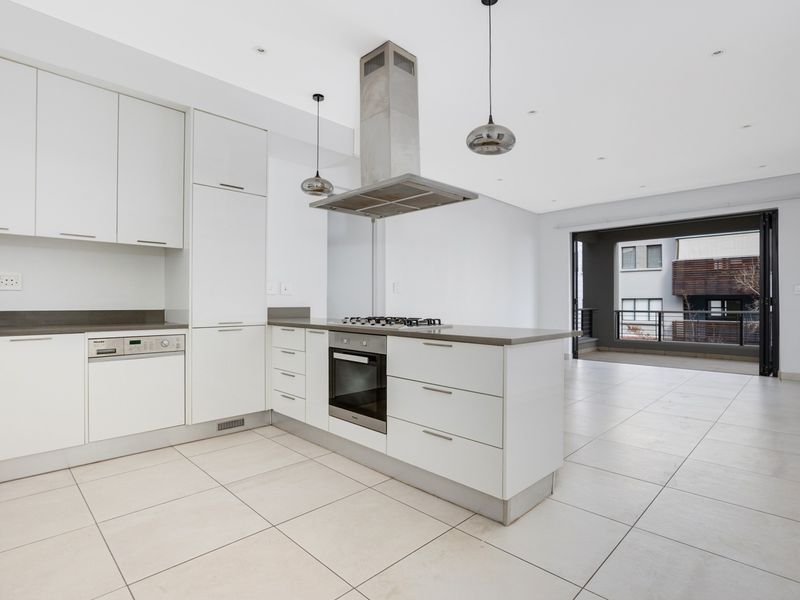Modern open-plan kitchen featuring sleek white cabinetry, integrated appliances, and stone countertops, flowing seamlessly into a bright living area with access to a private balcony.