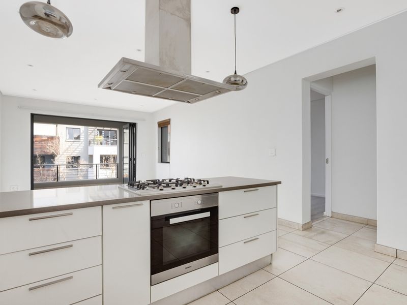 Modern kitchen featuring a central island with a gas hob, built-in oven, stainless steel extractor fan, stone countertops, and neutral tiled flooring.