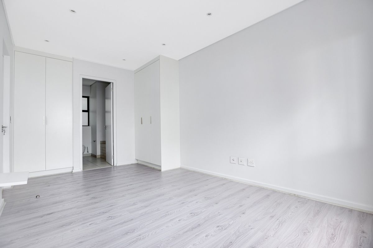A bright, empty bedroom featuring modern laminate flooring, built-in cupboards, and recessed downlighting, offering a clean and neutral space ready for personalization.