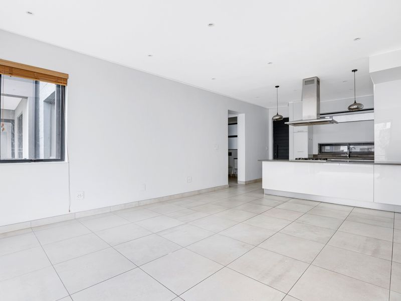 Spacious open-plan living area featuring modern tiled flooring, recessed lighting, and a sleek kitchen with a central island and stainless steel extractor fan.
