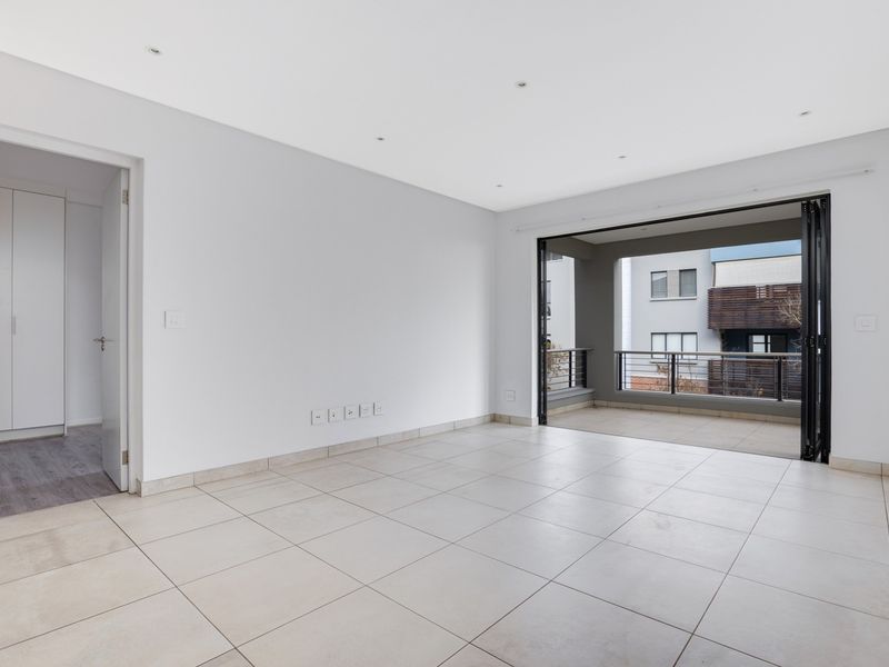 Bright and spacious open-plan living area featuring neutral tiled flooring, recessed lighting, and large bi-fold doors leading to a private balcony.