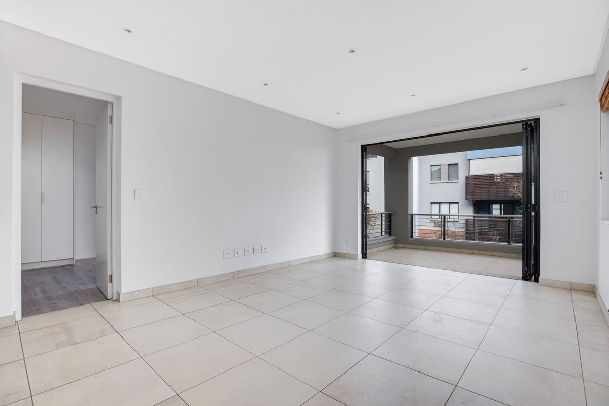 Bright and spacious open-plan living area featuring neutral tiled flooring, recessed lighting, and large bi-fold doors leading to a private balcony.