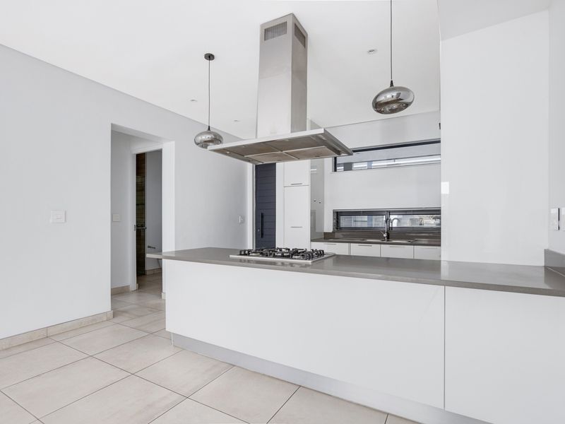 Modern kitchen featuring a central island with a gas hob, stainless steel extractor fan, sleek white cabinetry, and stone countertops.