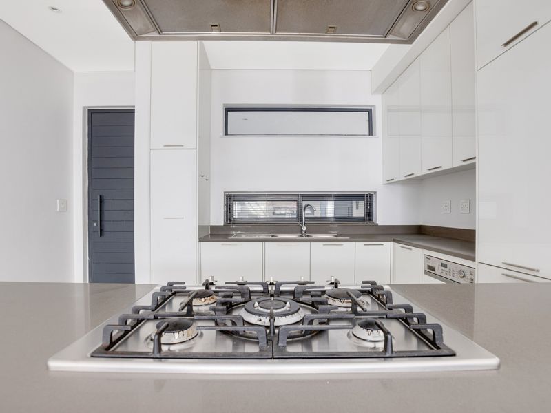 Modern kitchen featuring sleek white cabinetry, stone countertops, a gas hob with overhead extractor, and integrated appliances in a clean, minimalist design.