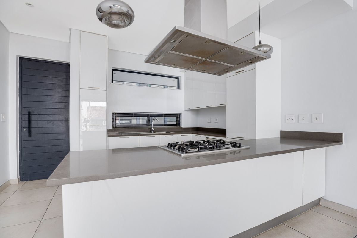 Modern kitchen featuring white cabinetry, stone countertops, a central gas hob with an overhead extractor fan, and a sleek undermount sink.