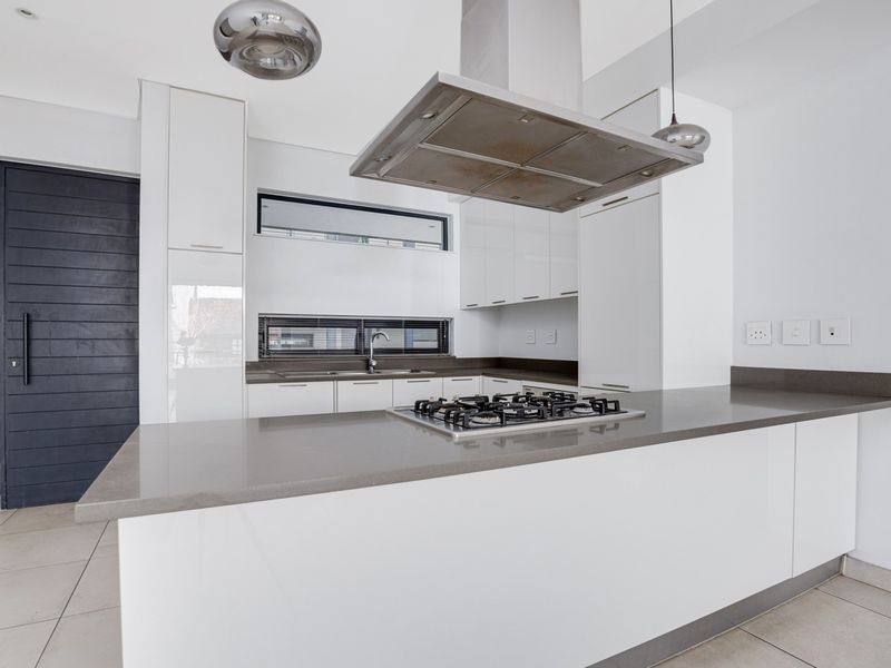 Modern kitchen featuring white cabinetry, stone countertops, a central gas hob with an overhead extractor fan, and a sleek undermount sink.