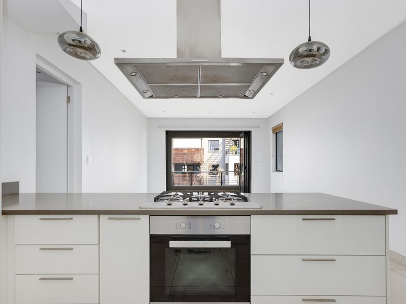 Modern kitchen featuring a central island with a gas cooktop, built-in oven, stainless steel extractor fan, and sleek white cabinetry with stone countertops.