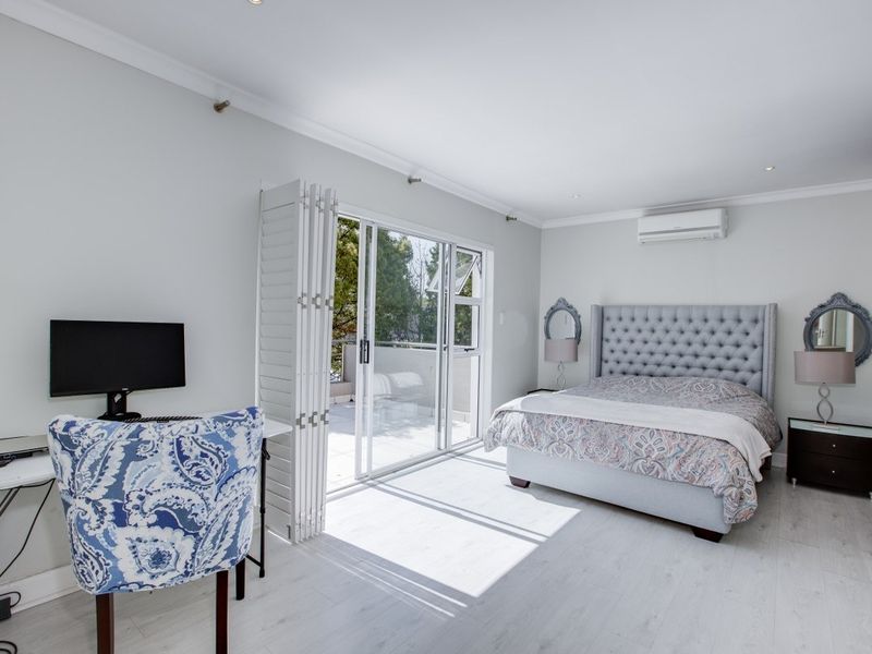 Spacious bedroom featuring light laminate flooring, recessed lighting, a wall-mounted air conditioner, and direct access to a private balcony through sliding glass doors.