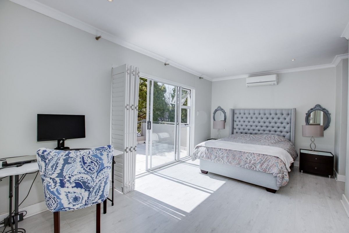 Spacious bedroom featuring light laminate flooring, recessed lighting, a wall-mounted air conditioner, and direct access to a private balcony through sliding glass doors.