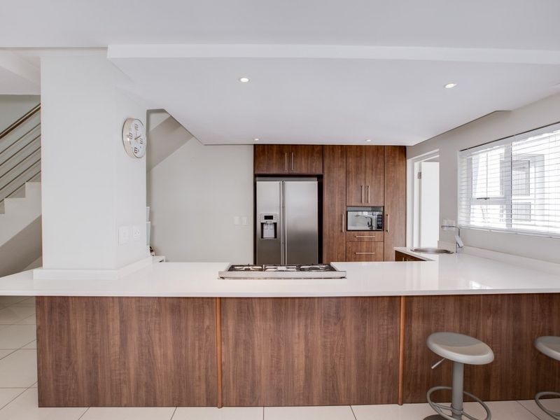 Modern kitchen featuring wood-finish cabinetry, stone countertops, a central gas hob, and integrated appliances, seamlessly connected to the living area and staircase.