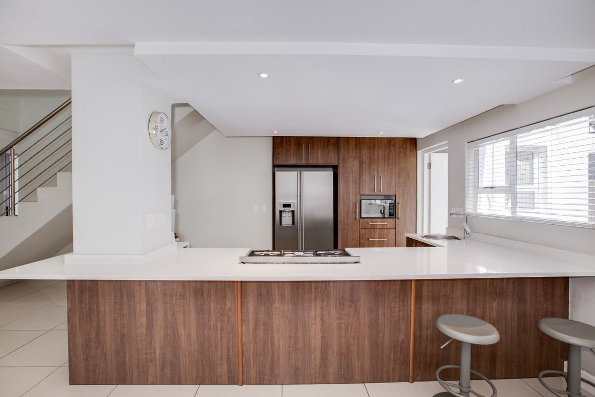 Modern kitchen featuring wood-finish cabinetry, stone countertops, a central gas hob, and integrated appliances, seamlessly connected to the living area and staircase.