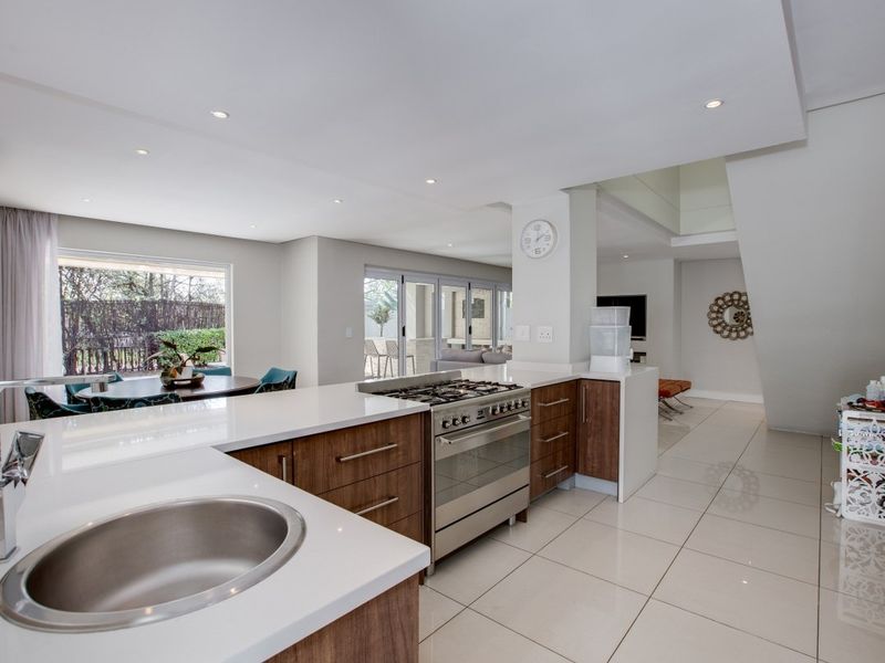 Modern open-plan kitchen featuring wood-finish cabinetry, quartz countertops, a gas stove, and tiled flooring, seamlessly flowing into the dining and living areas.