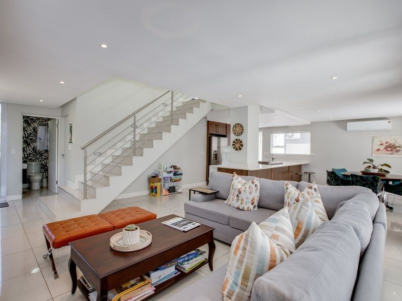 Spacious open-plan living area featuring a modern staircase with stainless steel balustrade, tiled flooring, recessed lighting, and an integrated kitchen with a central island.