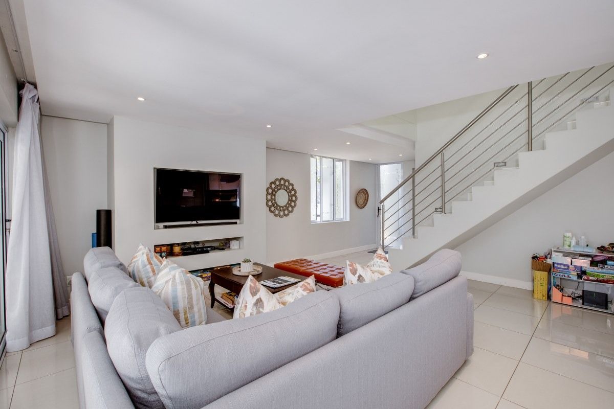 Modern open-plan living area featuring tiled flooring, recessed lighting, and a sleek staircase with a stainless steel balustrade.