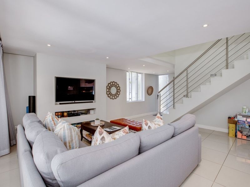 Modern open-plan living area featuring tiled flooring, recessed lighting, and a sleek staircase with a stainless steel balustrade.