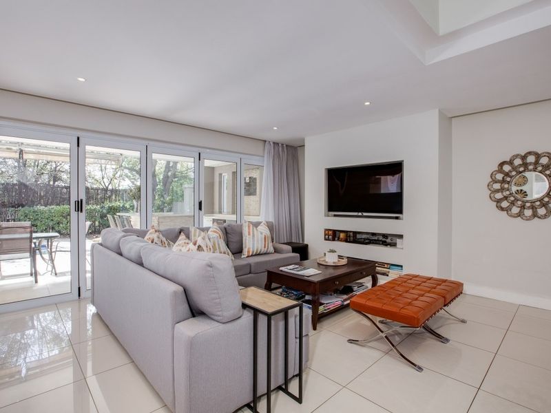 A bright and modern living room featuring large sliding glass doors, tiled flooring, recessed lighting, and a built-in media wall.