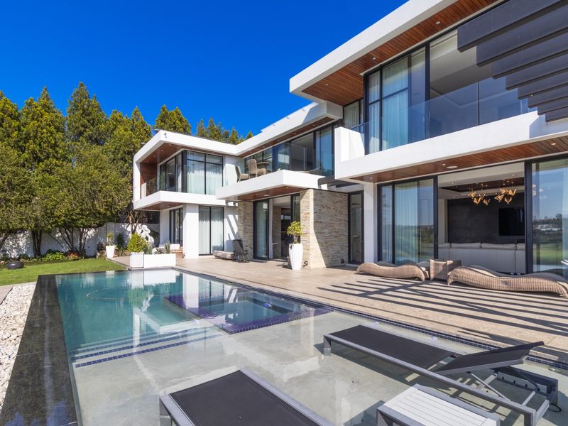 Modern luxury residence featuring a sleek swimming pool, expansive tiled patio, and contemporary architectural design with large glass sliding doors.