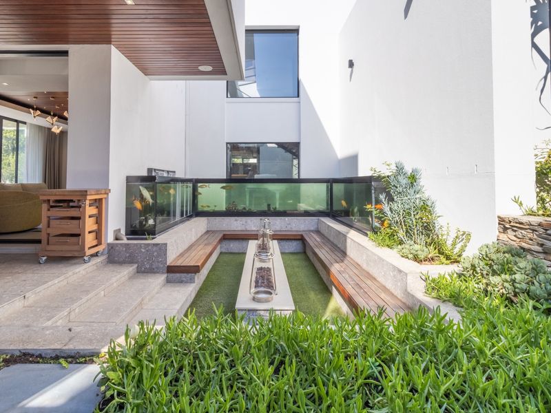 Modern outdoor patio featuring a sunken fire pit area, built-in timber seating, and a unique integrated aquarium wall, seamlessly connecting to the interior living space.