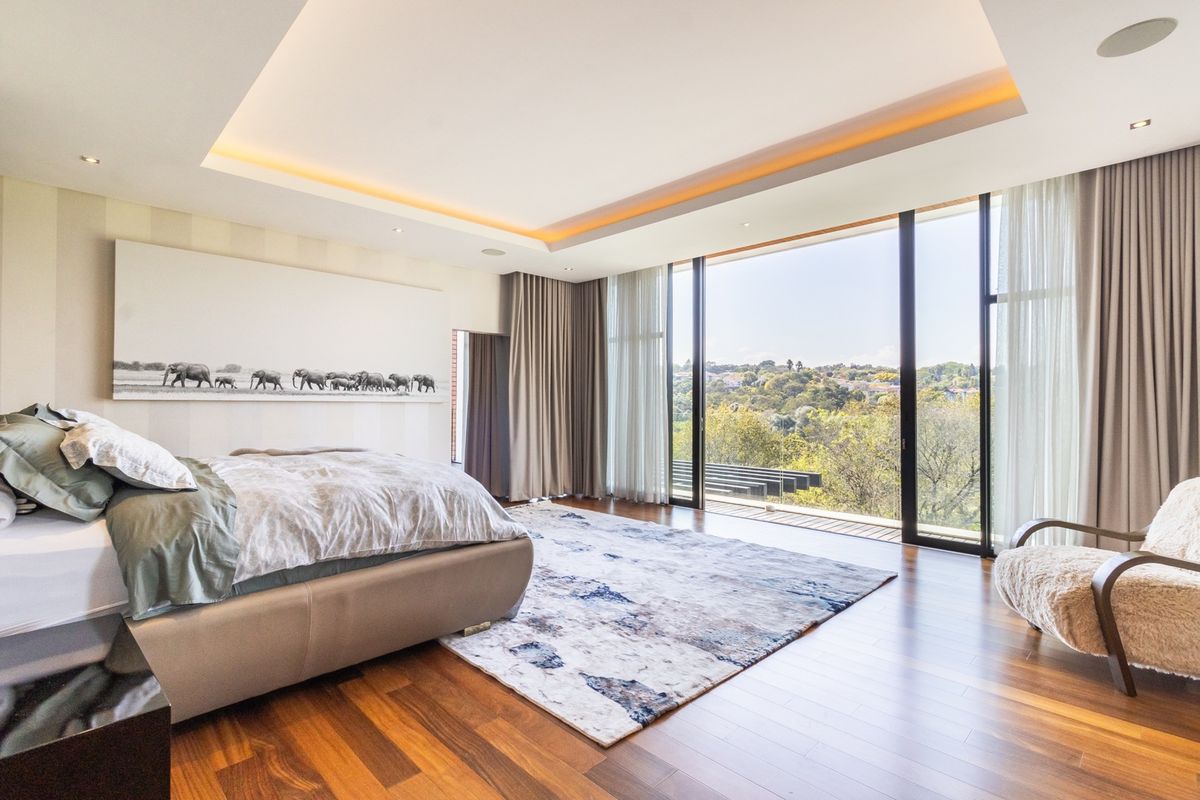 Spacious primary bedroom featuring hardwood flooring, recessed cove lighting, and expansive floor-to-ceiling glass doors opening to a scenic outdoor view.