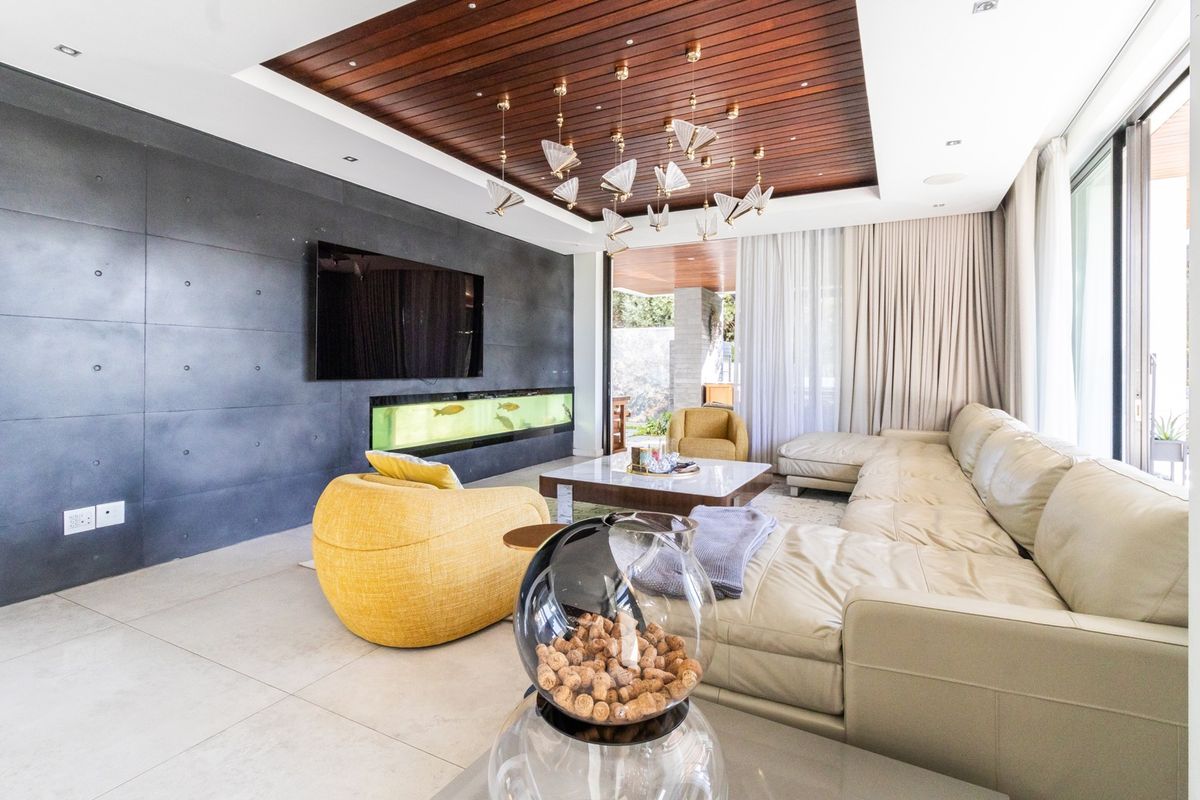 Modern living room featuring a striking timber-paneled recessed ceiling, a dark feature wall with an integrated aquarium, and large sliding doors opening to the outdoors.