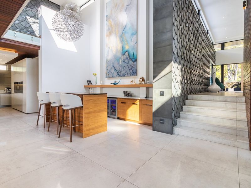 Spacious open-plan living area featuring high-end finishes, a custom built-in bar, textured feature wall, and elegant stone staircase with glass balustrade.