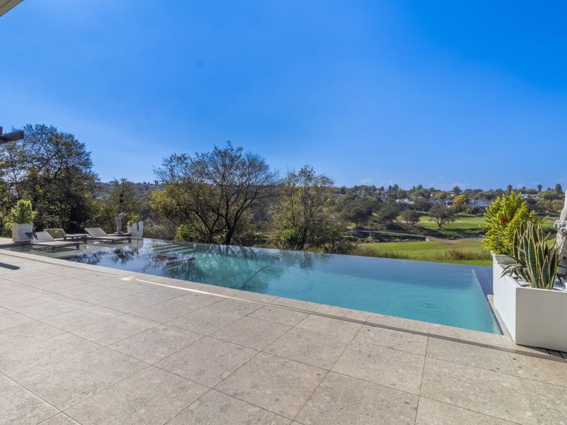 An elegant infinity edge swimming pool set on a spacious stone-tiled patio, offering expansive views over the surrounding landscape and golf course.