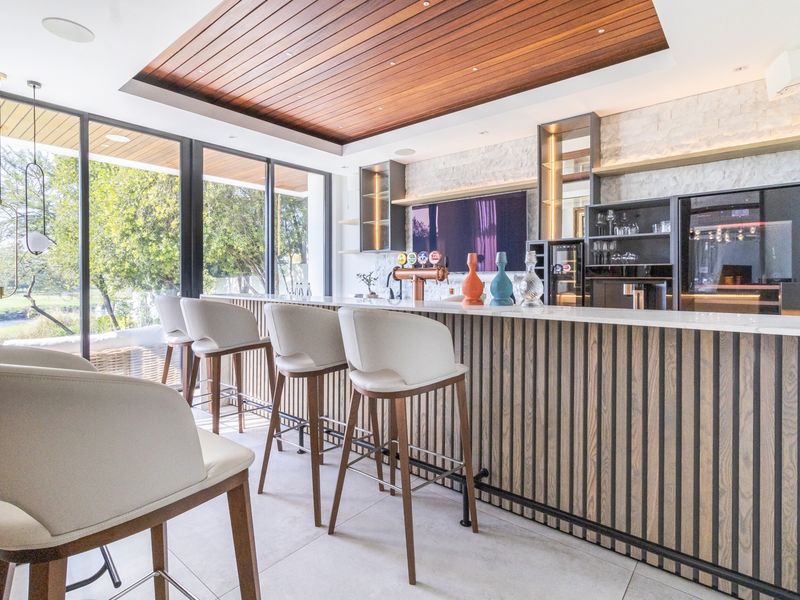Modern luxury home bar featuring a timber-clad counter, stone feature wall, integrated beverage refrigeration, and large sliding glass doors opening to the outdoors.