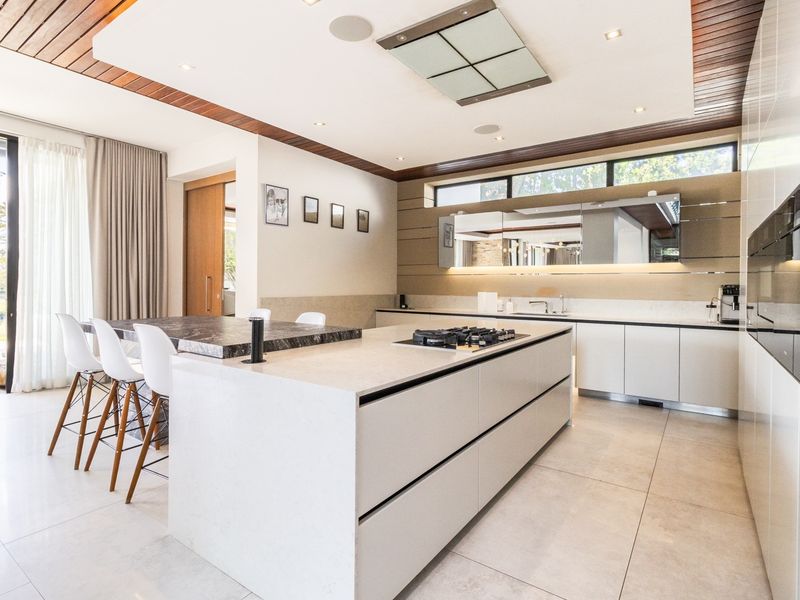 Modern, high-end kitchen featuring a large stone island with integrated gas cooktop, sleek cabinetry, and premium finishes with direct access to outdoor space.