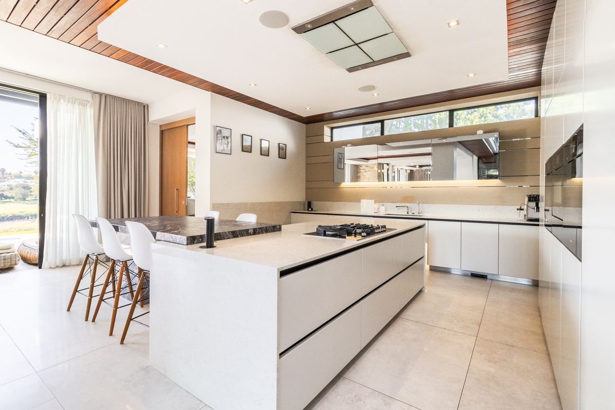 Modern, high-end kitchen featuring a large stone island with integrated gas cooktop, sleek cabinetry, and premium finishes with direct access to outdoor space.