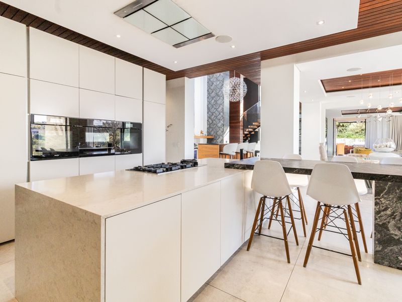 Modern open-plan kitchen featuring a large stone island, integrated appliances, sleek cabinetry, and elegant timber ceiling accents flowing into the living area.