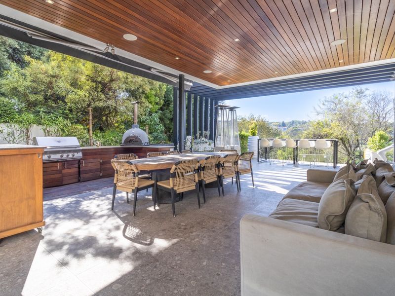 A spacious covered outdoor patio featuring a timber-clad ceiling, built-in kitchen with pizza oven, and stone flooring, ideal for alfresco dining and entertaining.
