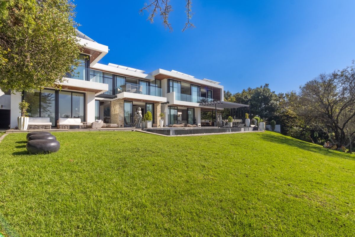 A modern luxury residence featuring a spacious rear lawn, an infinity-style swimming pool, and expansive glass sliding doors opening onto a covered patio area.