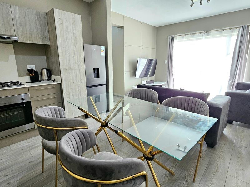 Modern open-plan living area featuring a contemporary kitchen with built-in appliances, laminate flooring, and seamless flow to the lounge space.