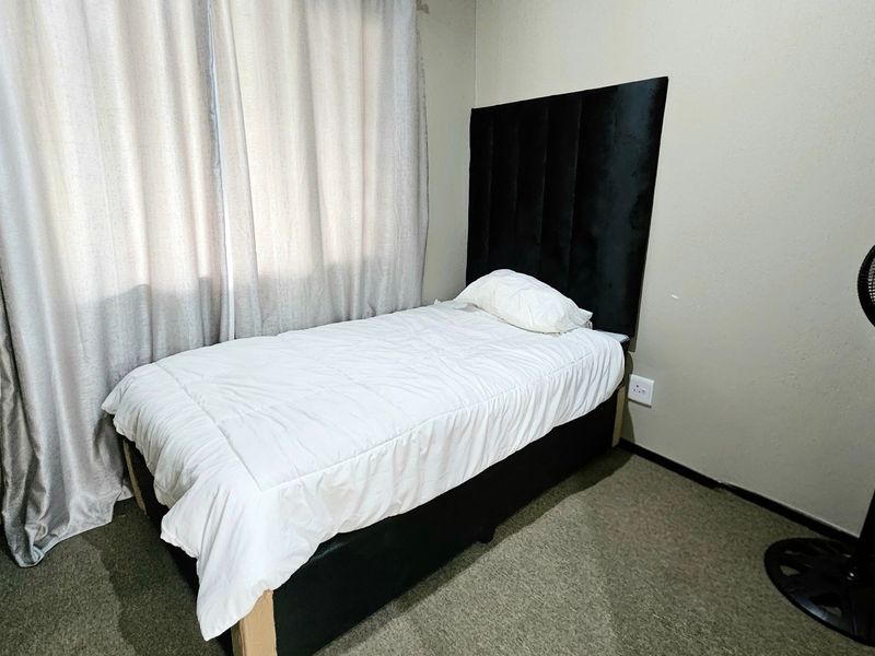 A compact bedroom featuring neutral wall finishes, carpeted flooring, and window curtain tracks.