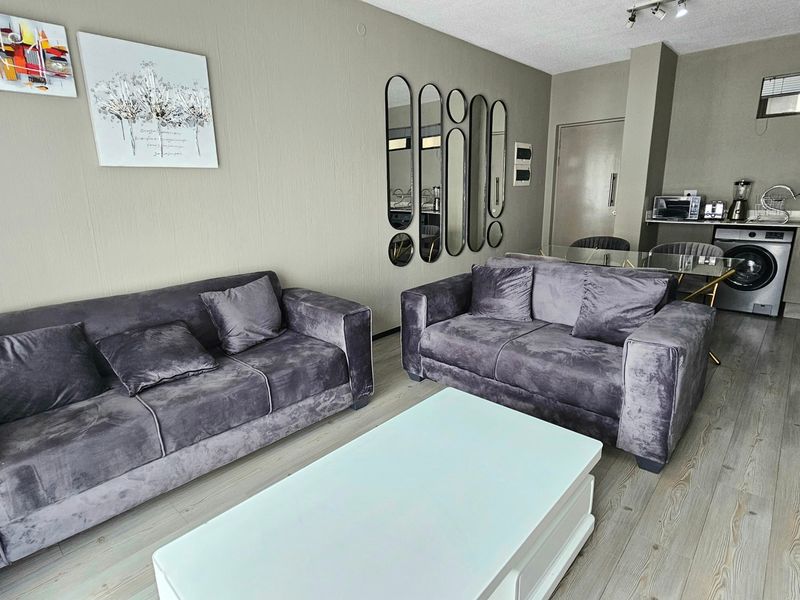 Open-plan living area featuring laminate flooring, neutral wall tones, and a compact kitchen space with integrated laundry plumbing.