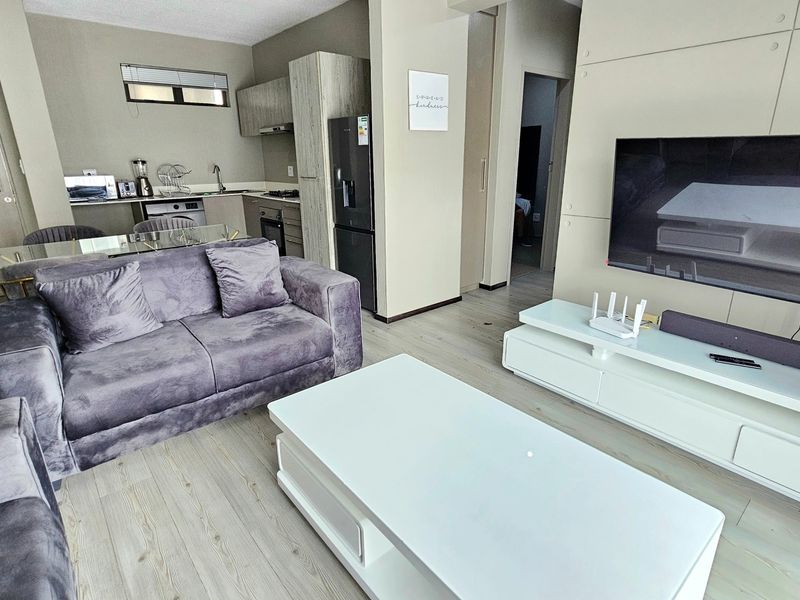 Modern open-plan living area featuring laminate flooring, a sleek built-in media wall, and a functional kitchen with integrated cabinetry and appliances.
