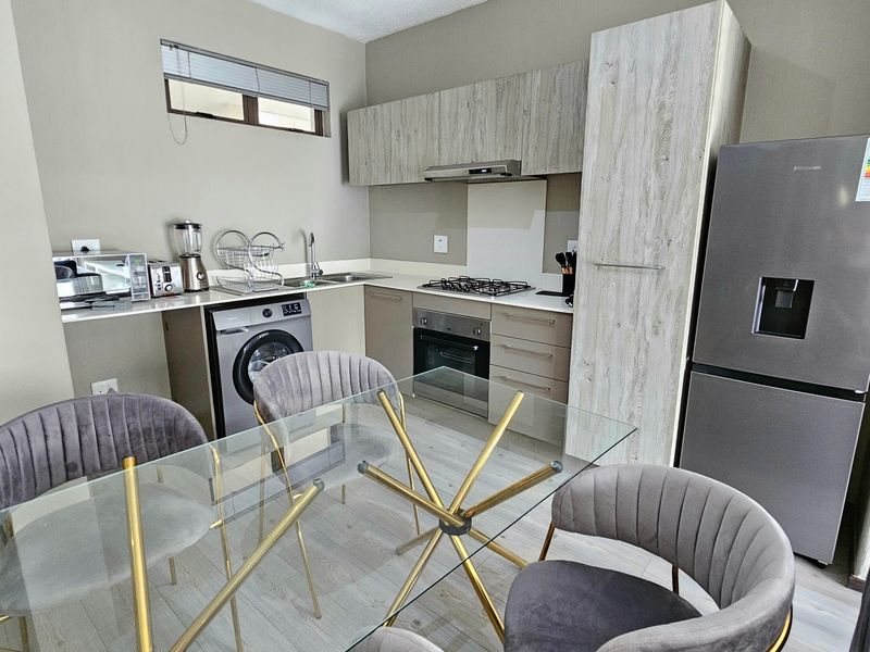Modern open-plan kitchen featuring light wood-grain cabinetry, integrated gas hob, oven, extractor fan, and durable laminate flooring in a contemporary apartment setting.