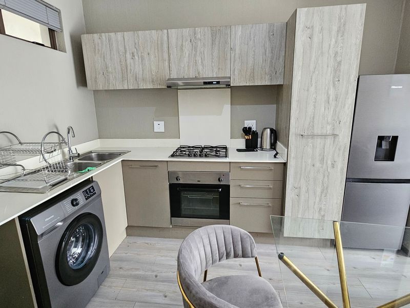 Modern kitchen featuring light wood-grain cabinetry, stone countertops, integrated gas hob, electric oven, and space for a washing machine.