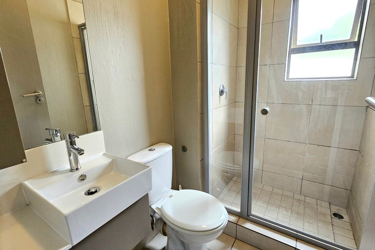 A functional bathroom featuring a modern vanity basin, toilet, and a glass-enclosed shower with tiled finishes throughout.
