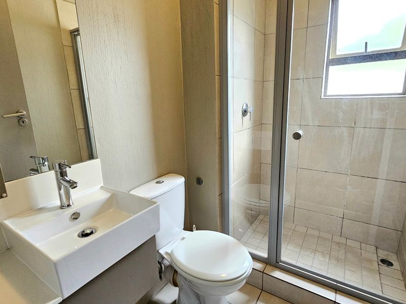 A functional bathroom featuring a modern vanity basin, toilet, and a glass-enclosed shower with tiled finishes throughout.