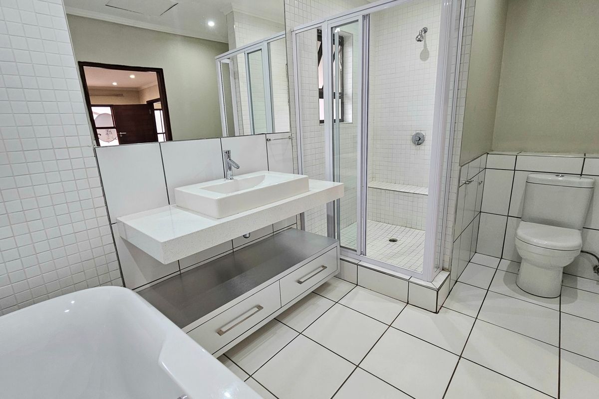 Modern bathroom featuring a floating vanity with vessel sink, a glass-enclosed shower with built-in bench, a bathtub, and neutral floor-to-ceiling tiling.
