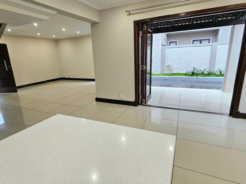 Spacious open-plan living area featuring large format floor tiles, recessed lighting, and bi-fold doors opening onto a private patio area.