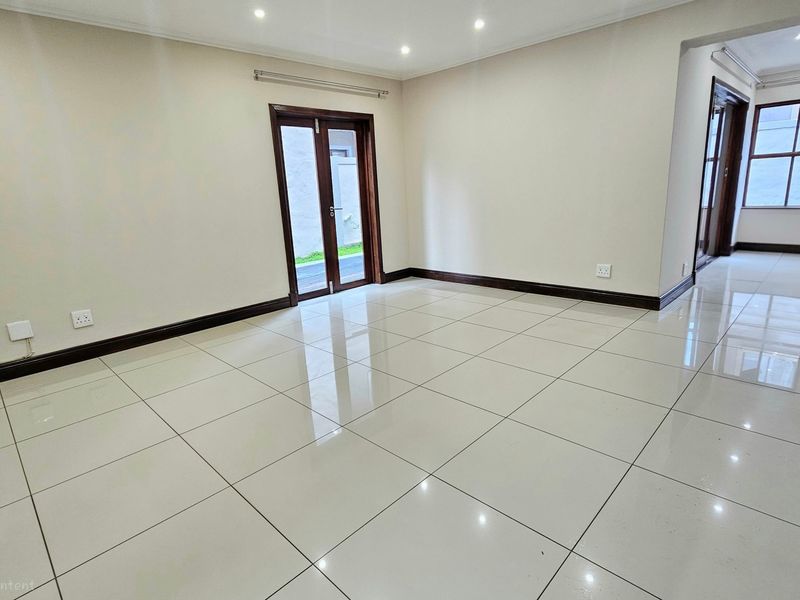 Spacious, light-filled living area featuring neutral walls, polished porcelain floor tiles, and direct access to the exterior through double glass doors.