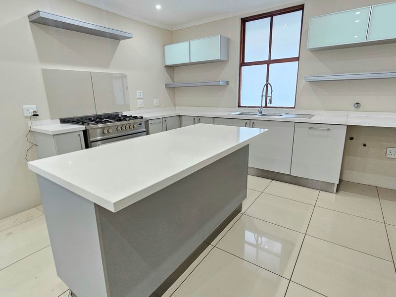 Modern kitchen featuring a central island, quartz countertops, gas stove with extractor, and ample built-in cabinetry with a clean, neutral aesthetic.