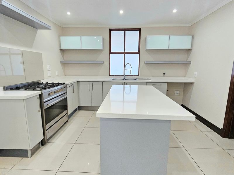 Modern kitchen featuring a central island, quartz countertops, gas stove with extractor, and ample built-in cabinetry with a clean, neutral aesthetic.