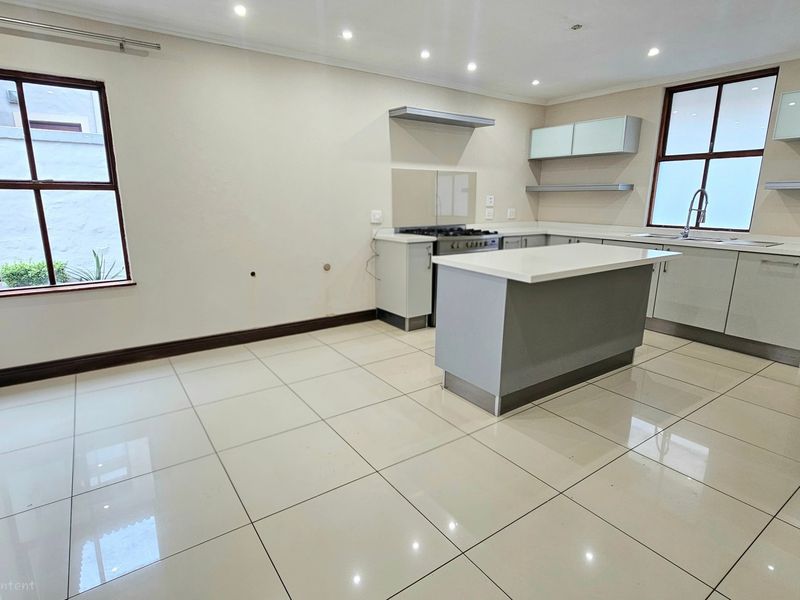 Modern, empty kitchen featuring a central island, gas stove, extractor fan, and sleek cabinetry with tiled flooring and recessed lighting.