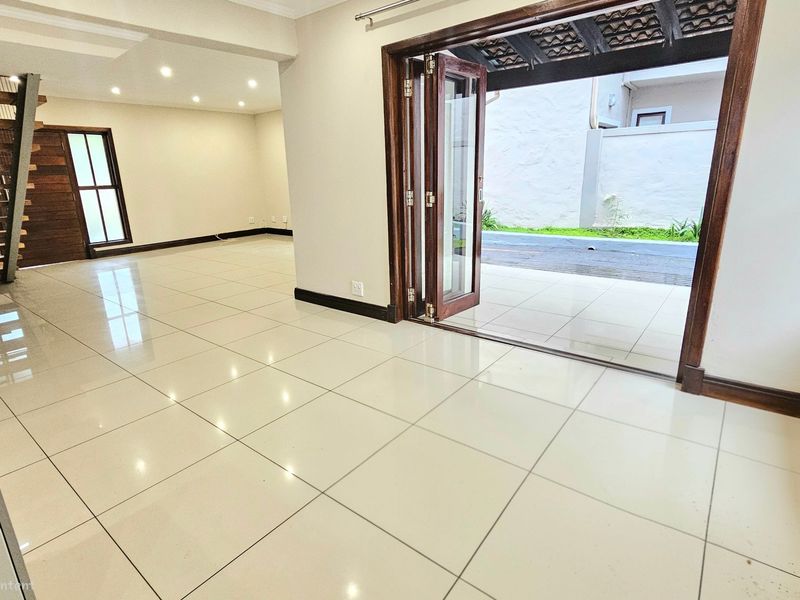 Spacious open-plan living area featuring polished tile floors, a modern wooden staircase, and bi-fold doors opening to an outdoor patio space.