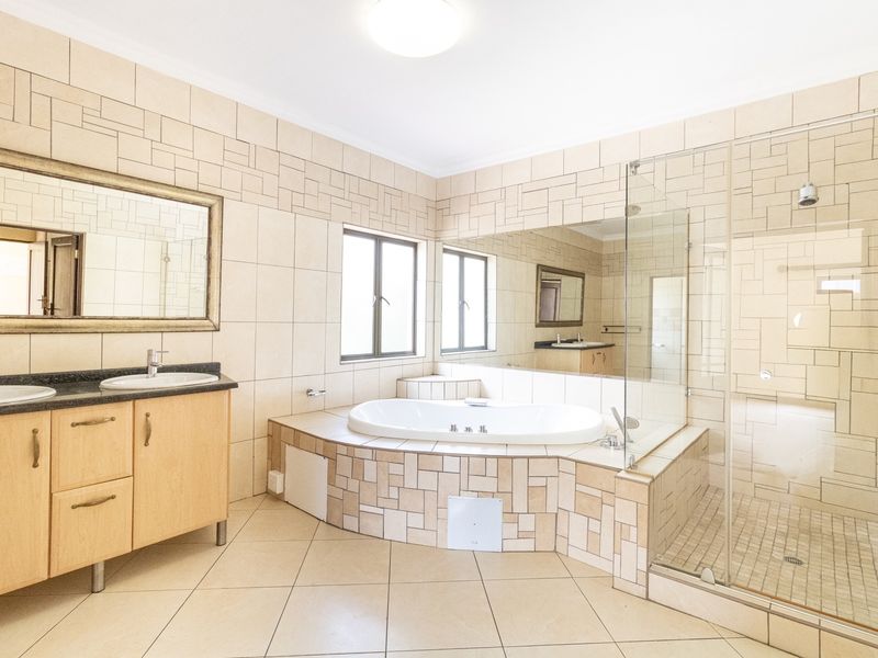 Spacious bathroom featuring a double vanity, a built-in bathtub, and a separate glass-enclosed shower with neutral tiled finishes throughout.