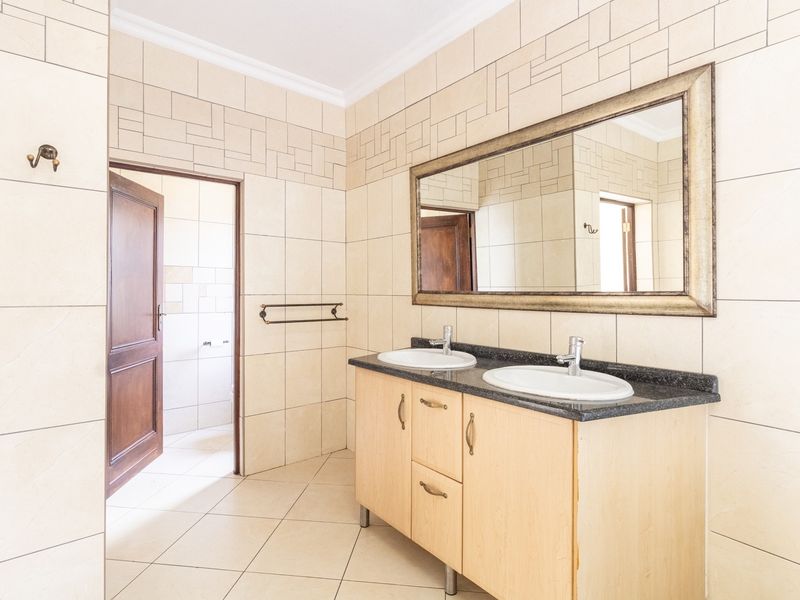 A spacious bathroom featuring a double vanity with granite countertop, neutral ceramic wall and floor tiles, and a large wall-mounted mirror.