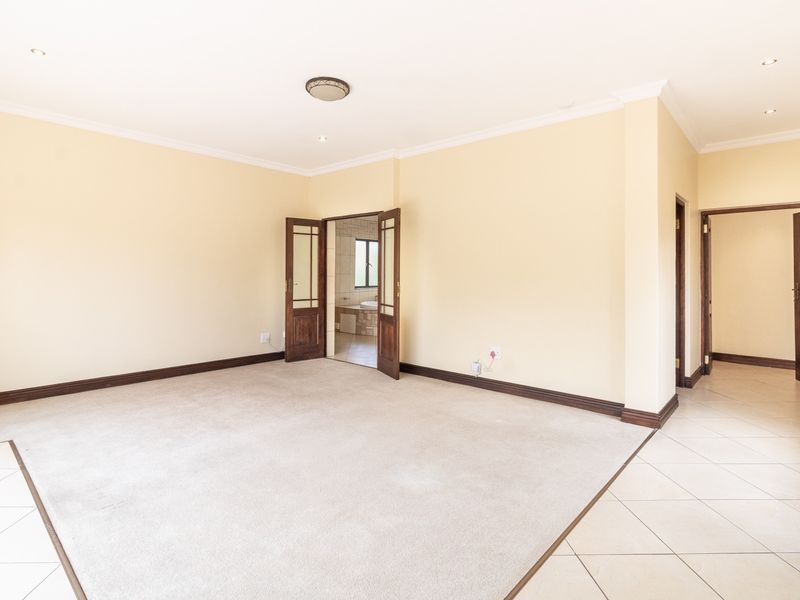 Spacious, empty bedroom featuring neutral carpet and tiled flooring, with direct access to an en-suite bathroom through double timber doors.